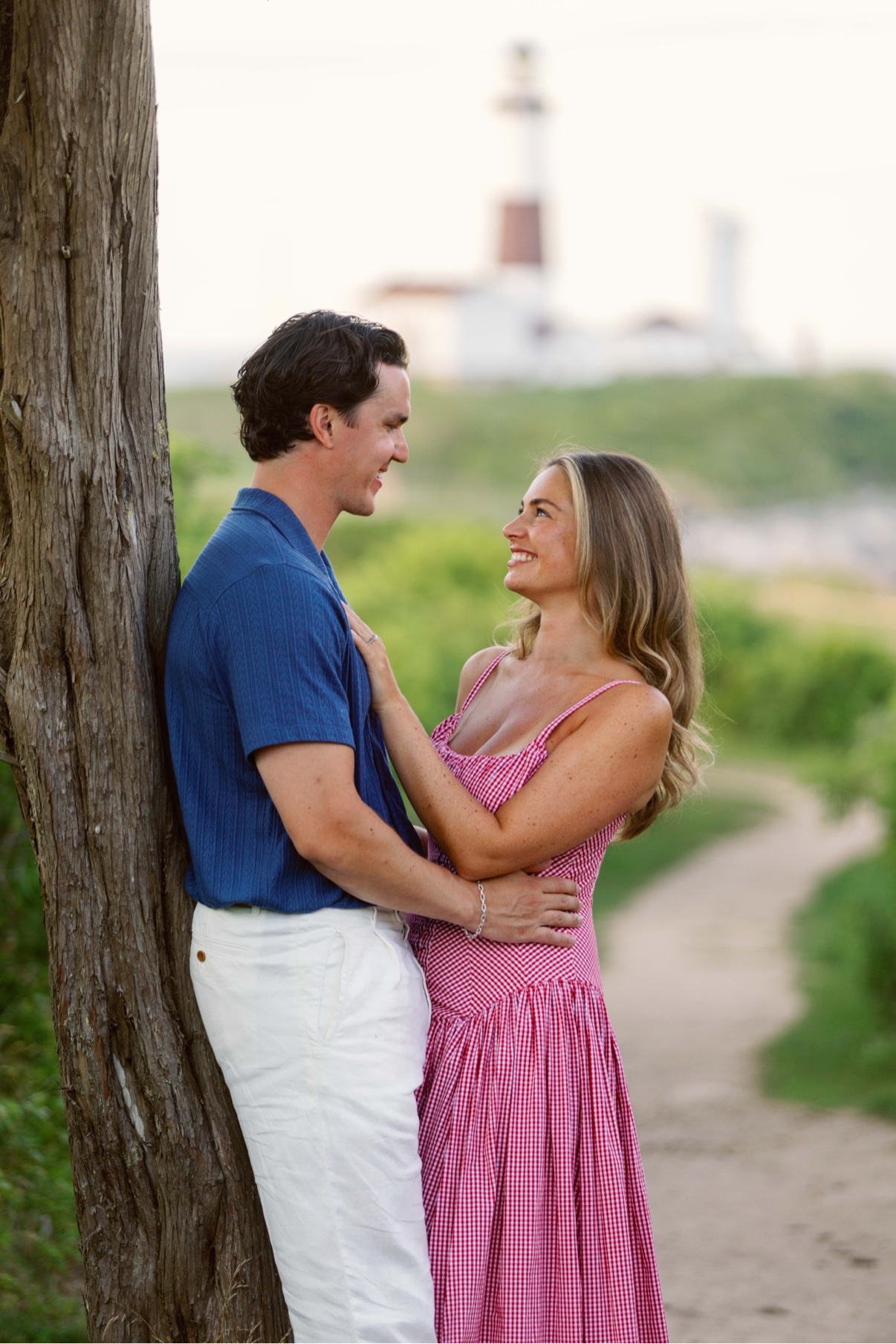 Couple embracing beside a tree with Montauk Lighthouse in the distance, Long Island