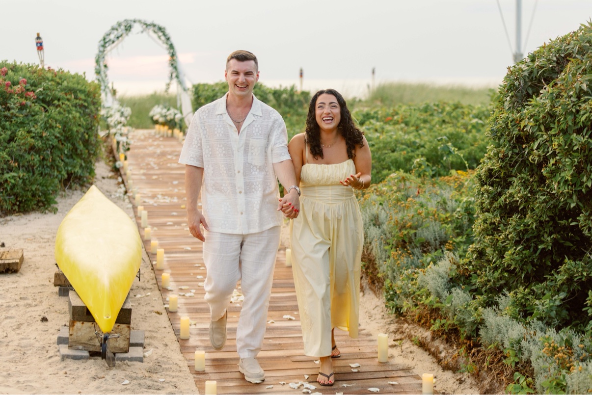 Couple walking hand in hand down a candlelit boardwalk path moments before a surprise proposal on Long Island