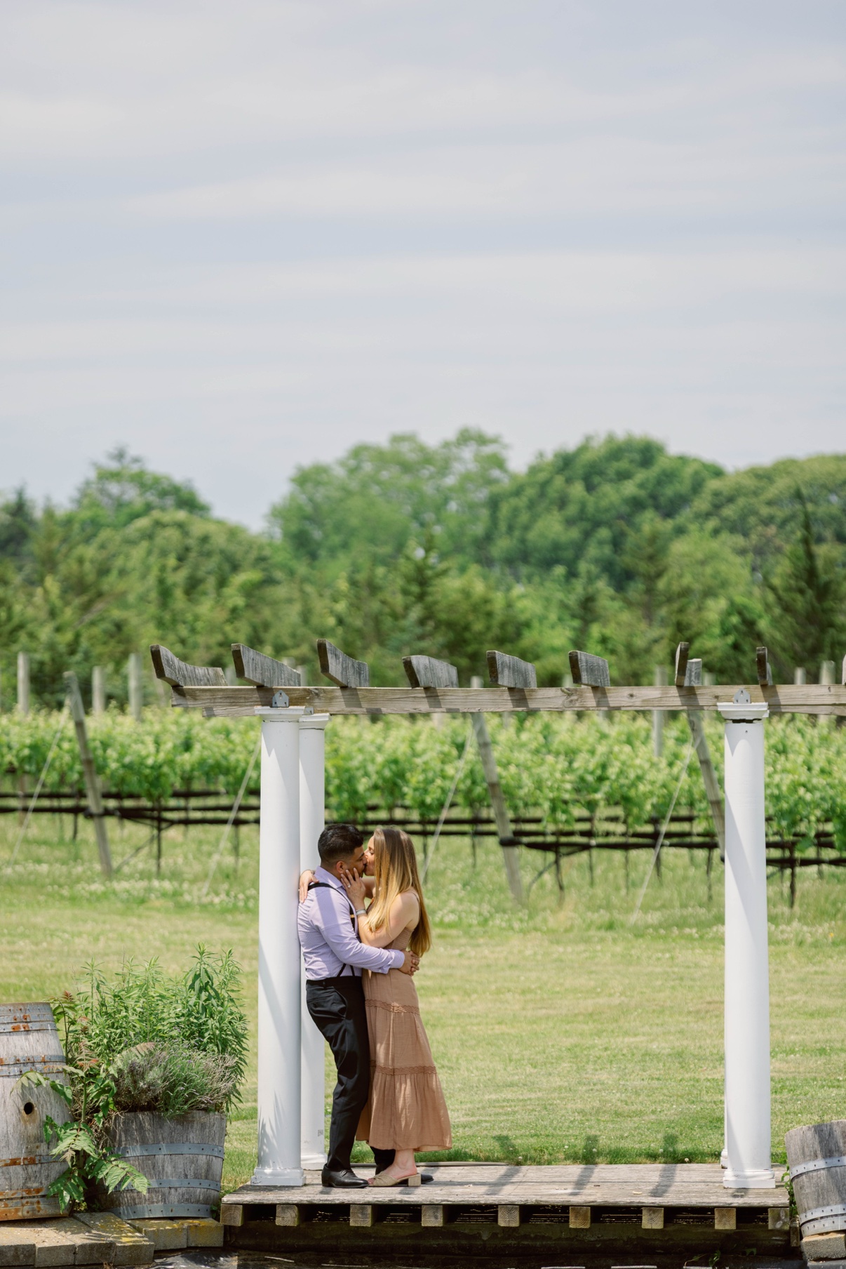 Engagement session at a North Fork vineyard — a couple embracing under the pergola