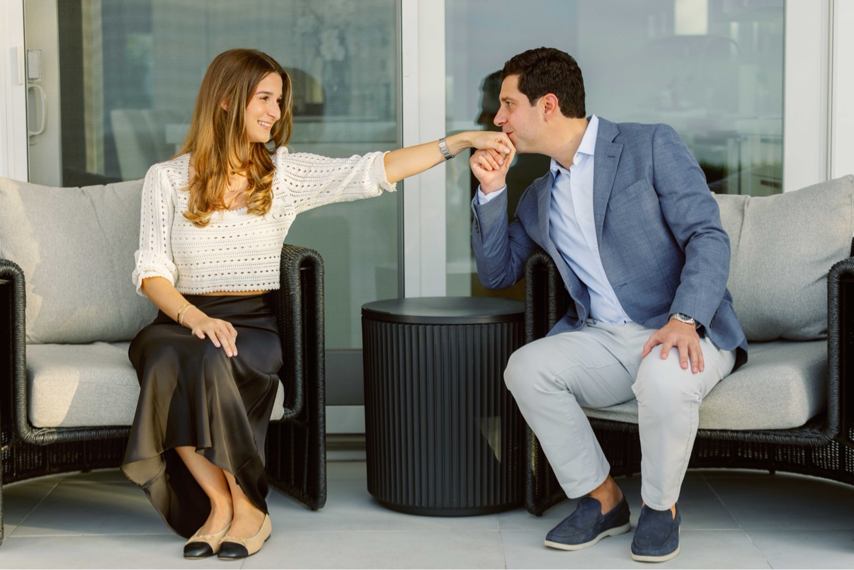 On the patio of a private Long Island beach house, he kisses her hand just after she said yes