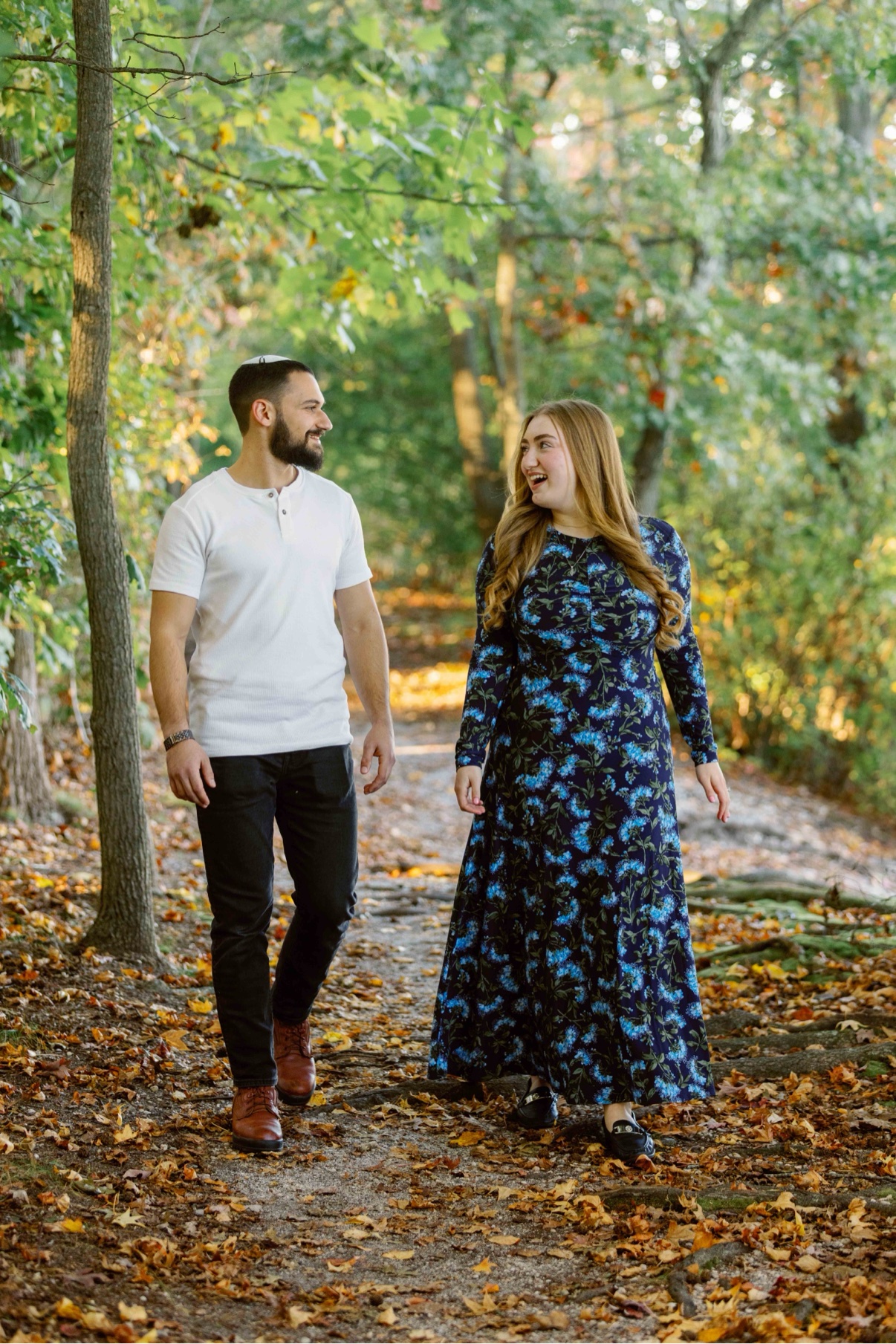Engagement photos at Twin Lakes Preserve, Wantagh, New York — a newly engaged couple walking hand in hand down the leaf-covered path, looking at each other