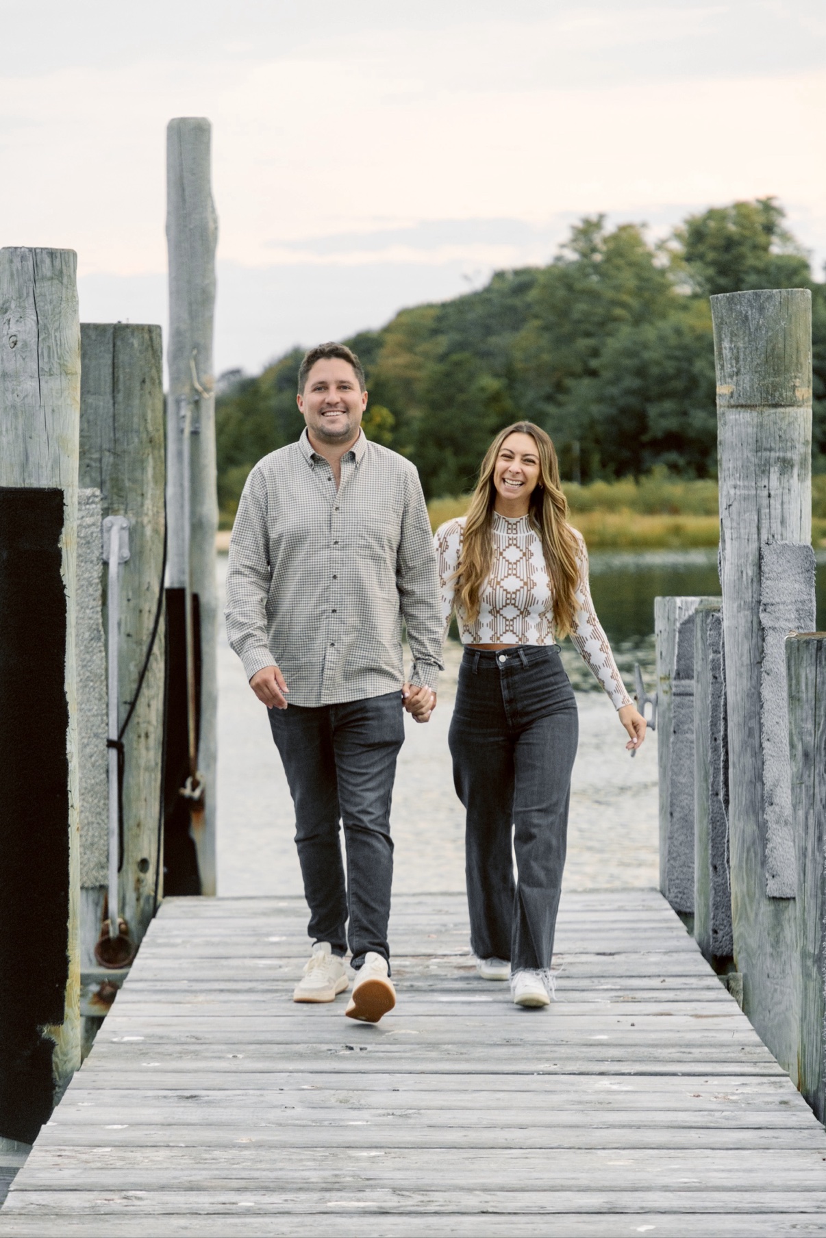 Engagement photos in Sag Harbor, Long Island — a couple walking hand in hand down the marina dock, laughing
