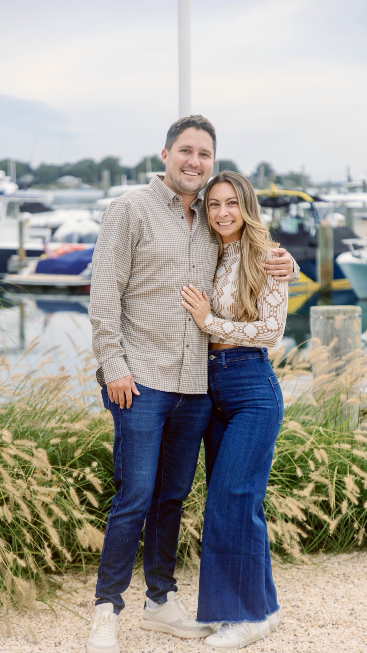Newly engaged couple posing together at the marina in Sag Harbor, Long Island, the boats behind them