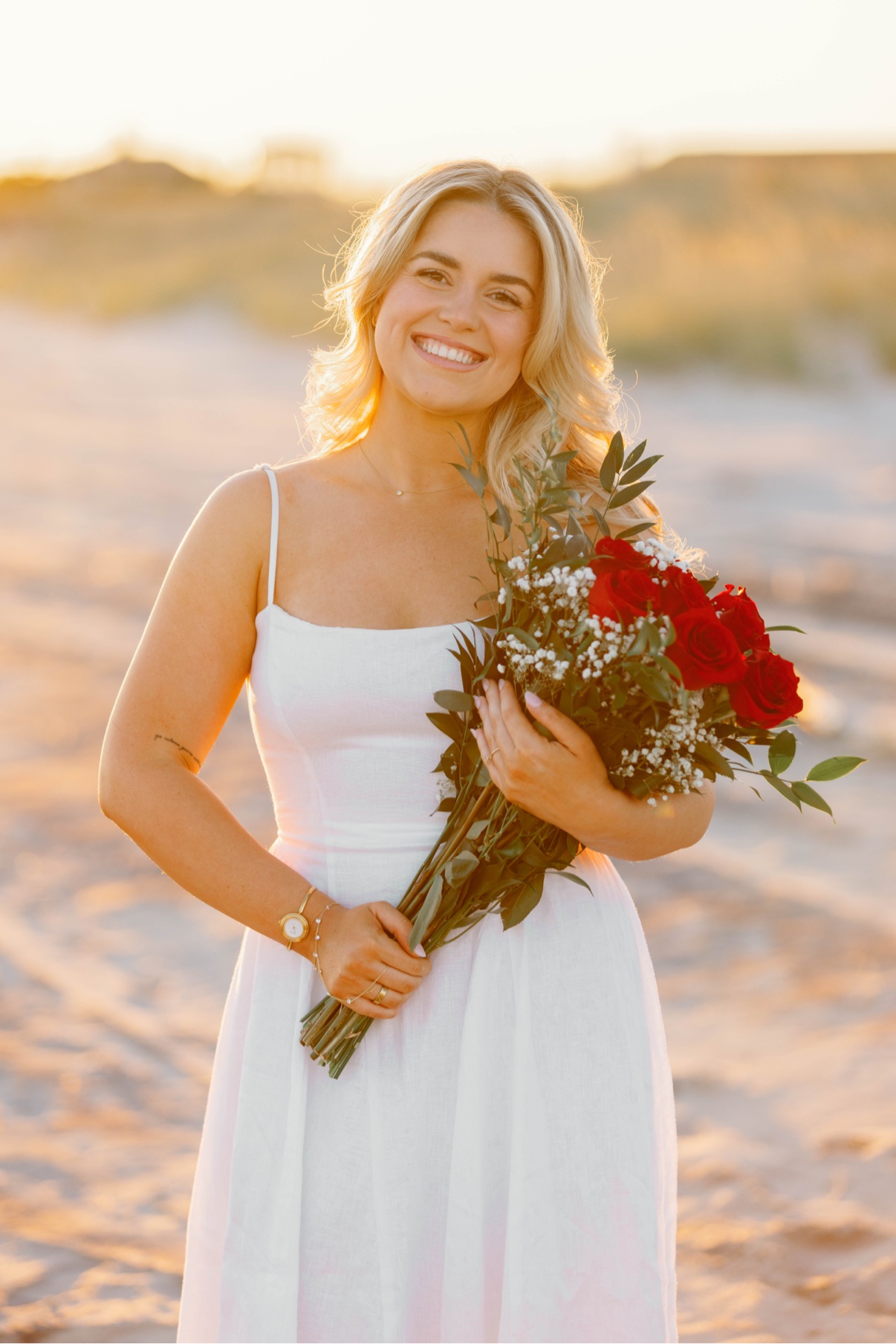 Engagement session at Cooper's Beach, Southampton, Long Island — a close-up of the bride-to-be smiling with her bouquet of red roses in the golden light