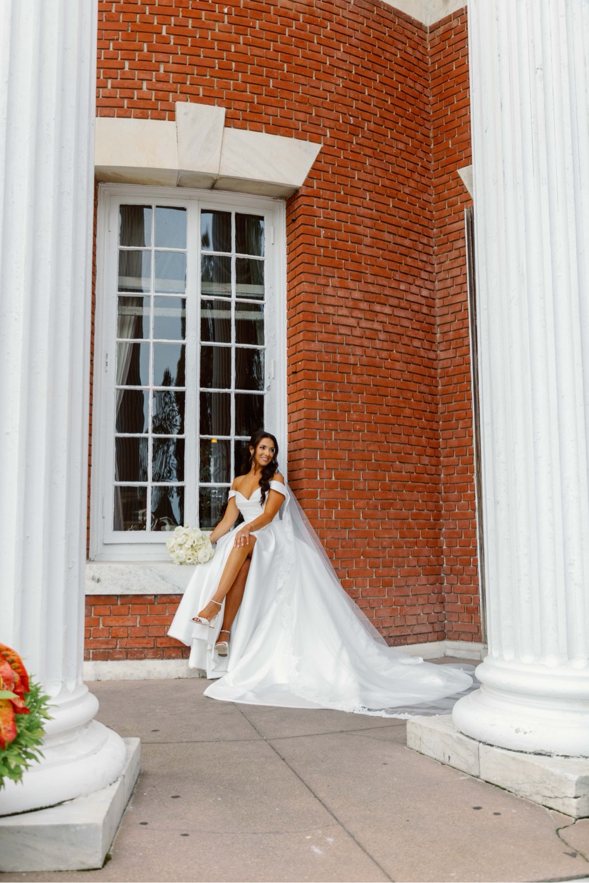 Bride posing beside the brick and white colonnade at Bourne Mansion