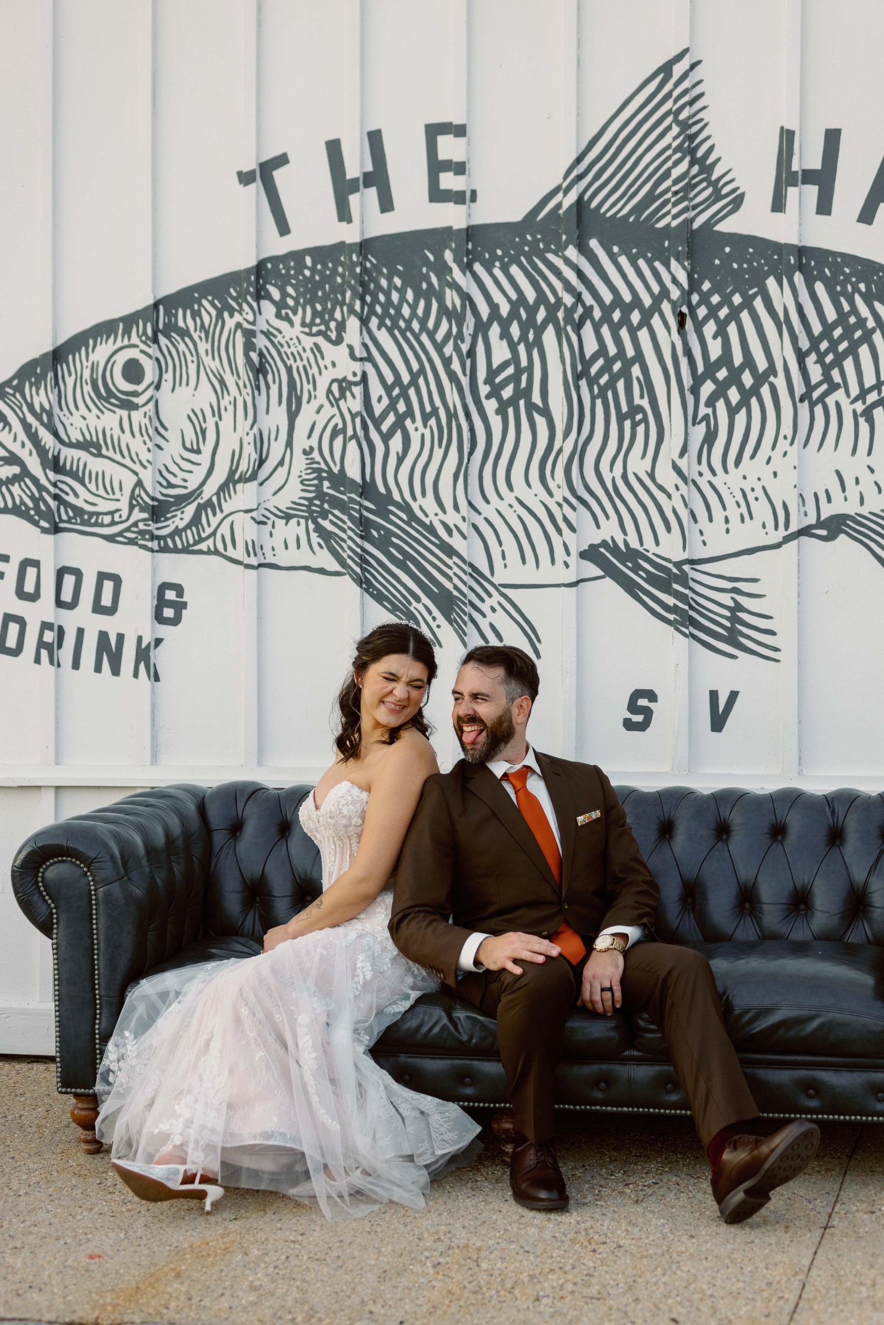 Bride and groom laughing together on a couch beneath a painted fish mural