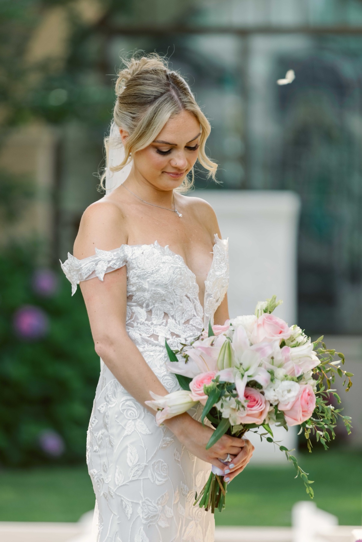 Samantha holding her bouquet with her eyes lowered in the gardens at The Muses