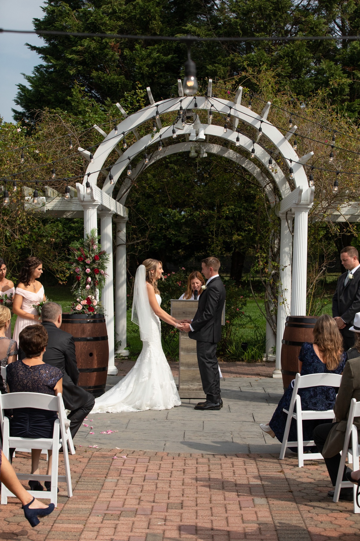 Bride and groom holding hands during their outdoor ceremony beneath a white pergola and string lights at a North Fork vineyard