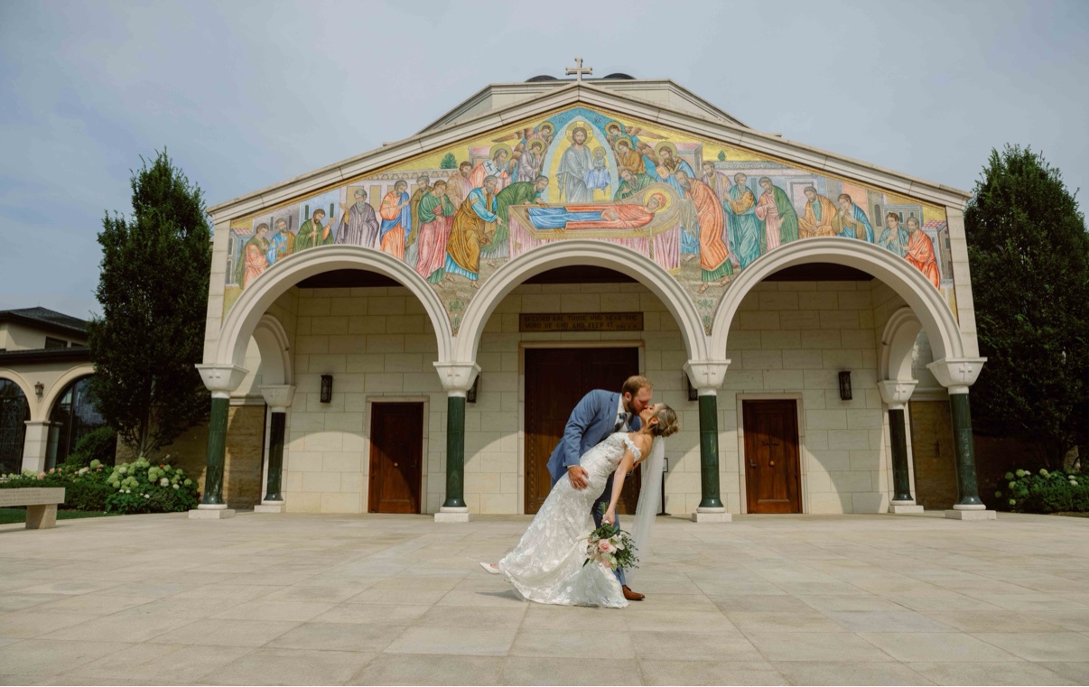 Bride and groom sharing a dip kiss in front of a mosaic church