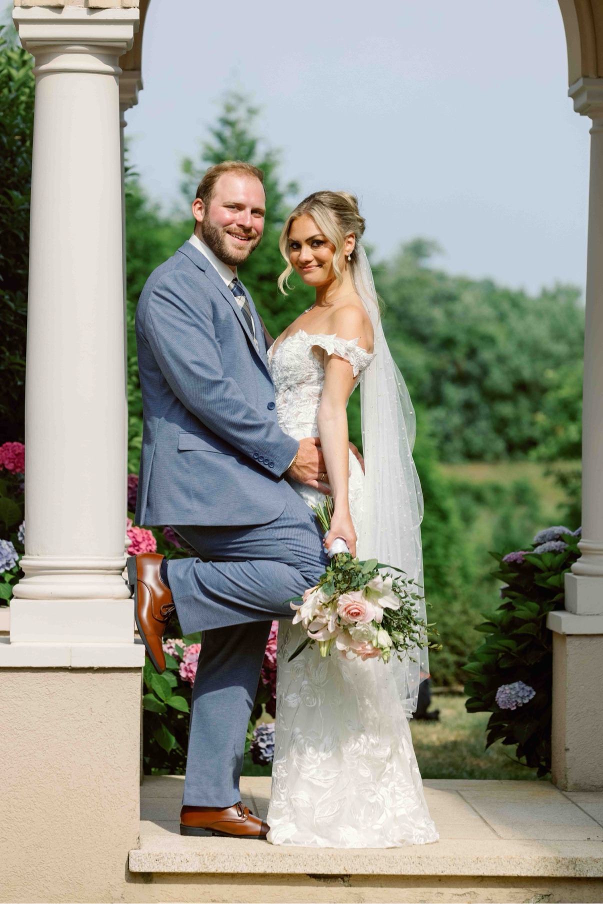 Bride and groom posed beside the white columns with her veil flowing at The Muses, Southampton — wedding photographer in Southampton